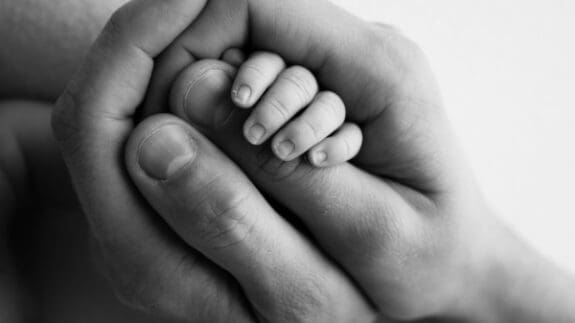 Black and white image of a adult hand holding a baby's hand