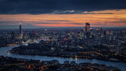 Wide aerial panorama of the illuminated London skyline during evening, England, with River Thames leading into the city