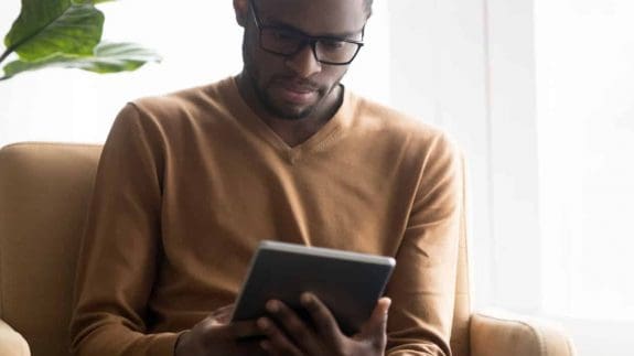 Focused African American man in glasses using tablet computer reading about Zero-rating for digital publications