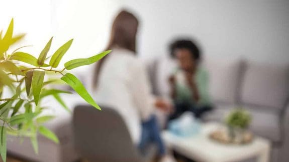 Two blurred figures sitting in an office discussing harassment with a plant in the foreground