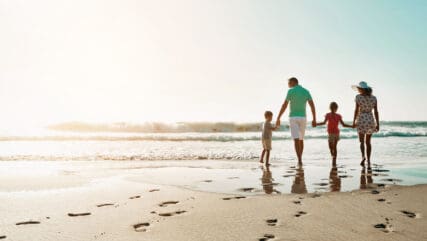 Family of four people walking on beach, relaxed, stress-free and happy.