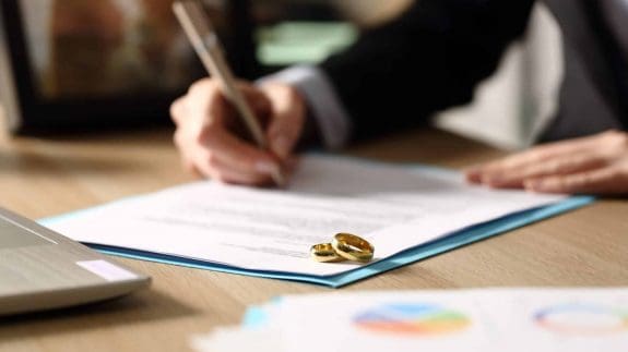 Close up of a person sitting at a desk signing a divorce legal document