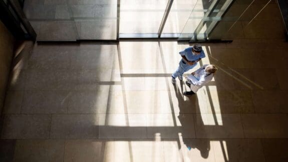 Aerial view of two NHS workers discussing pension changes in front of sun filled window