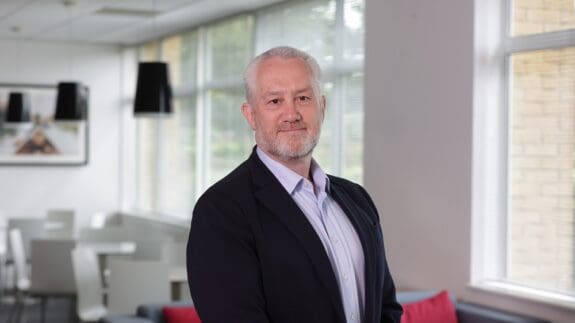 Greg Mayne standing in office smiling