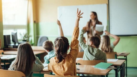 children in classroom with hands up