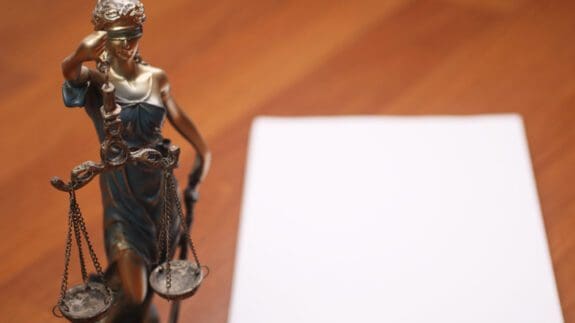 Justice statue on wooden table next to blank sheet of paper