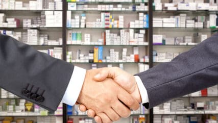 close up of shaking hands, pharmacy in background