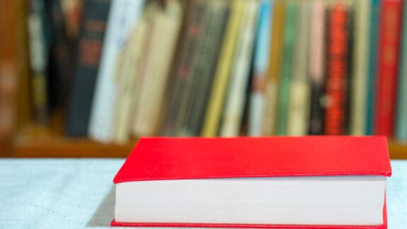 Red book on table with books on shelf in soft focus behind