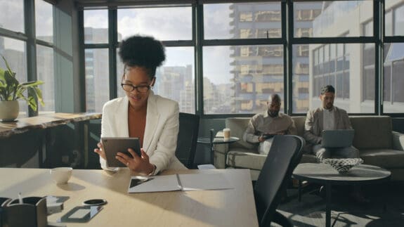 A business woman sitting at a desk in an office setting reviewing RSUs on a tablet