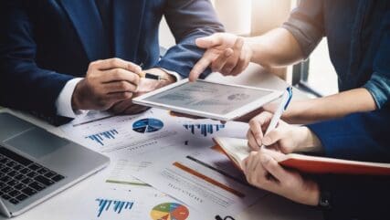 Three people in discussion over a table covered in pages of graphs and figures.