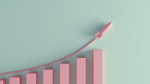 A pastel pink coloured growing graph with rising rocket on a green background.