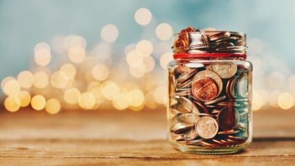 gift aid money jar filled with coins in front of holiday lights